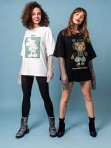 Two women pose stylishly in oversized graphic T-shirts, embodying modern fashion on a blue background.